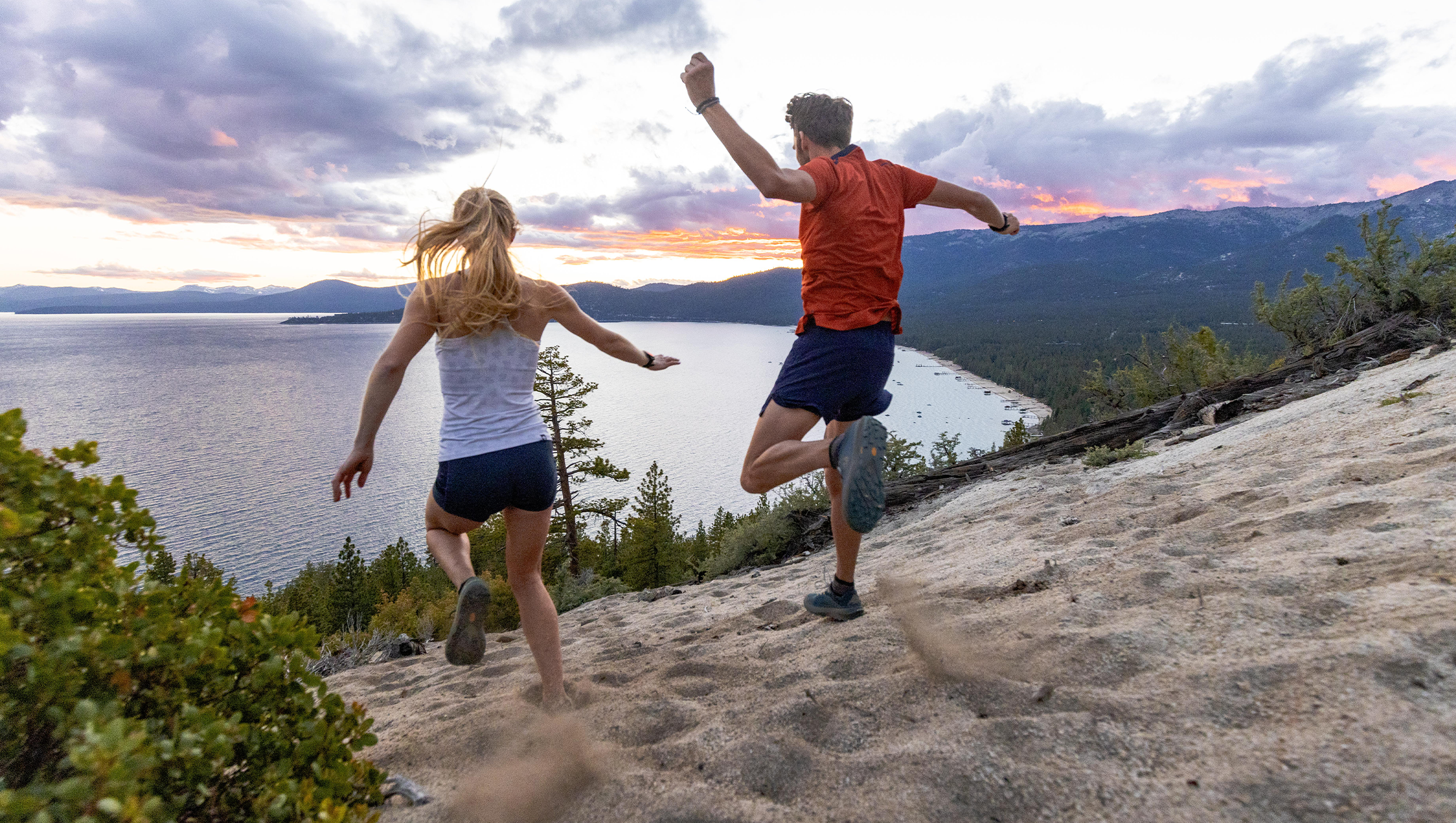 Decorative image for Topo Mission Statement. Two people running down a sandy hill that leads into a lake.